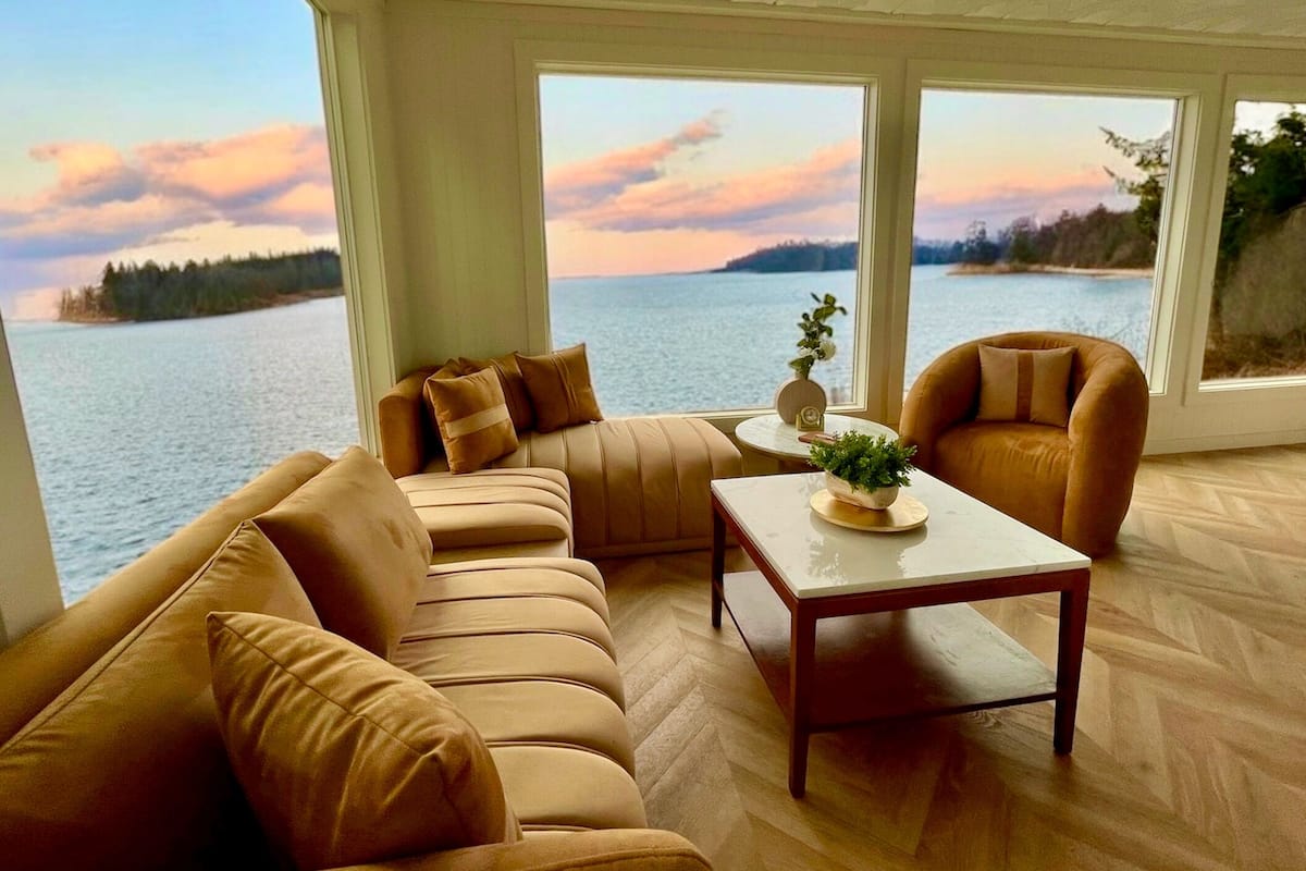 A living room with a large window overlooking a body of water and a sunset.