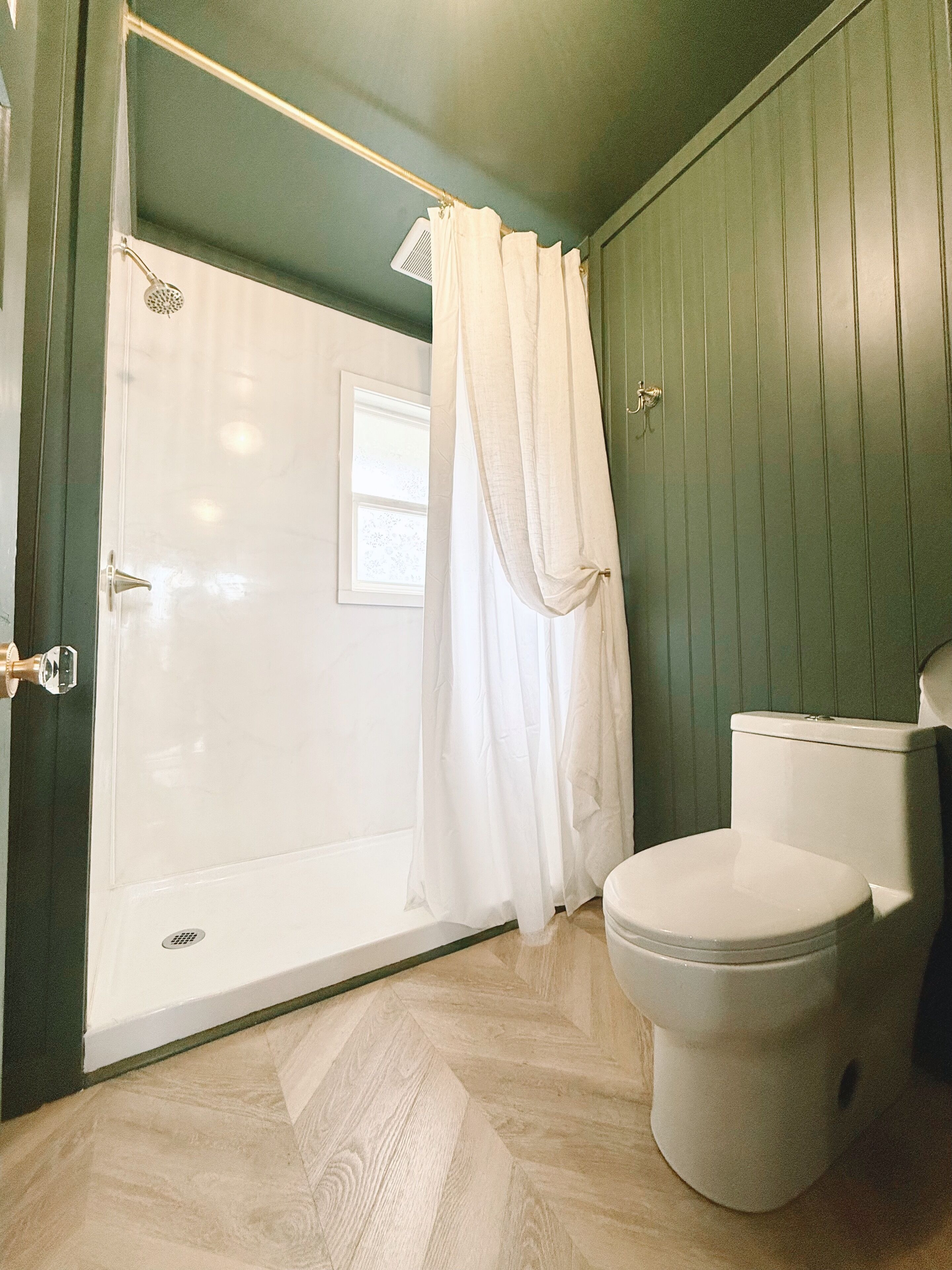 A bathroom with a shower, toilet, and a window.