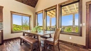 Un comedor con mesa y bancos de madera, ventanas amplias que dan a zonas verdes y techo de madera.