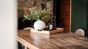 Une table en bois, sur laquelle sont posés un vase blanc et deux bouteilles de vin, le tout placé devant un mur de pierres et un panneau en bois.