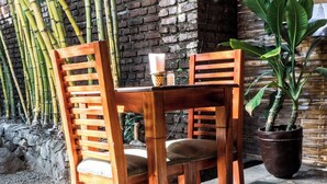 A wooden table and chairs set on a tiled floor with a brick wall and bamboo plants in the background. - PURE Gym - Spa - Yoga - Lodging (Granada)