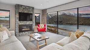 A modern living room with a stone fireplace, a red armchair, and a large window overlooking a mountainous landscape.