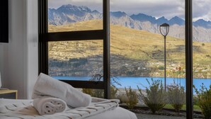 A bedroom with a large window overlooking a mountainous landscape and a lake.