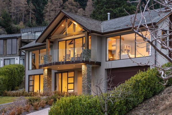A modern two-story house with a balcony, stone accents, and large windows.