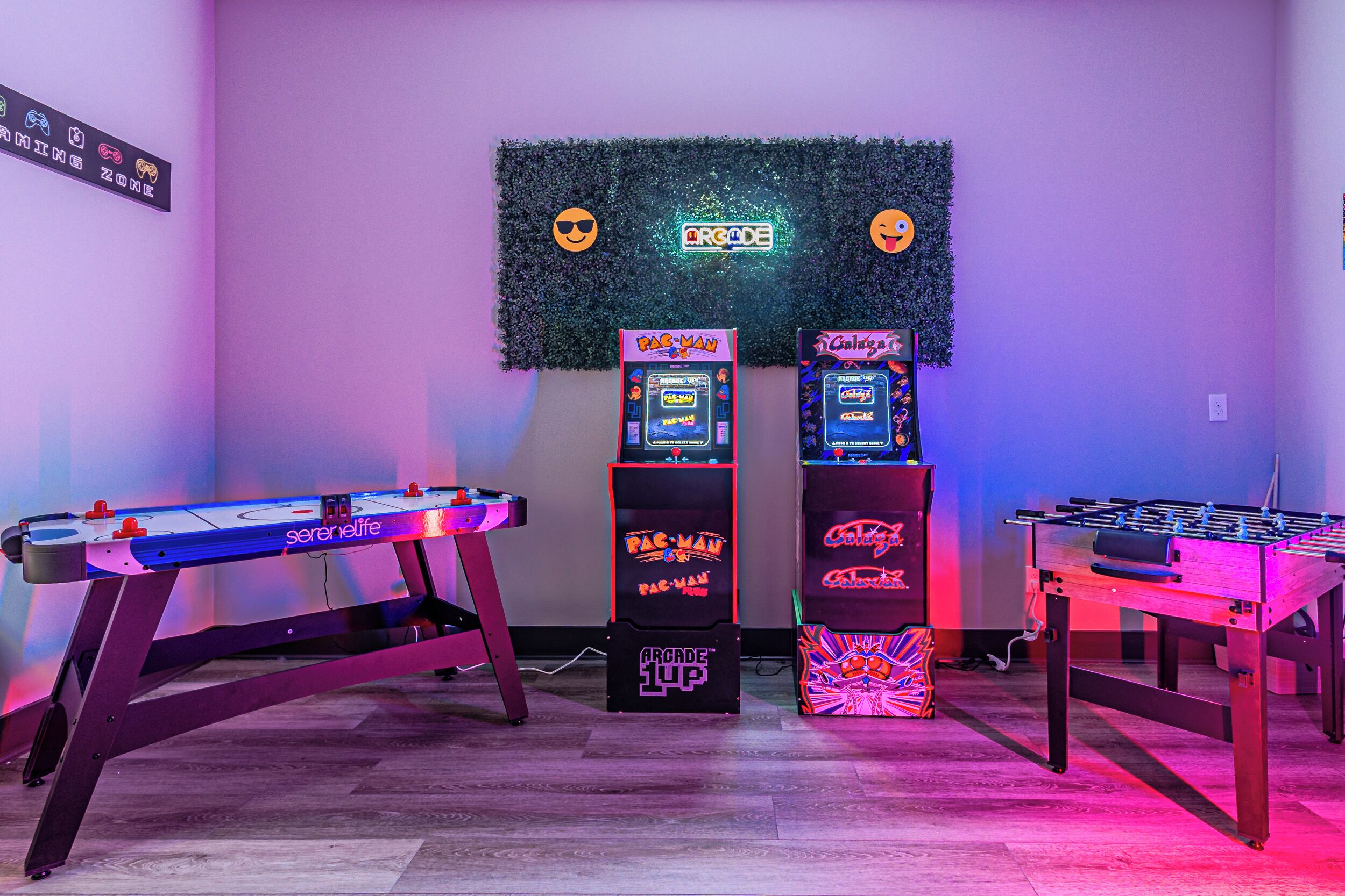 A room with two foosball tables, a karaoke machine, and arcade game machines.