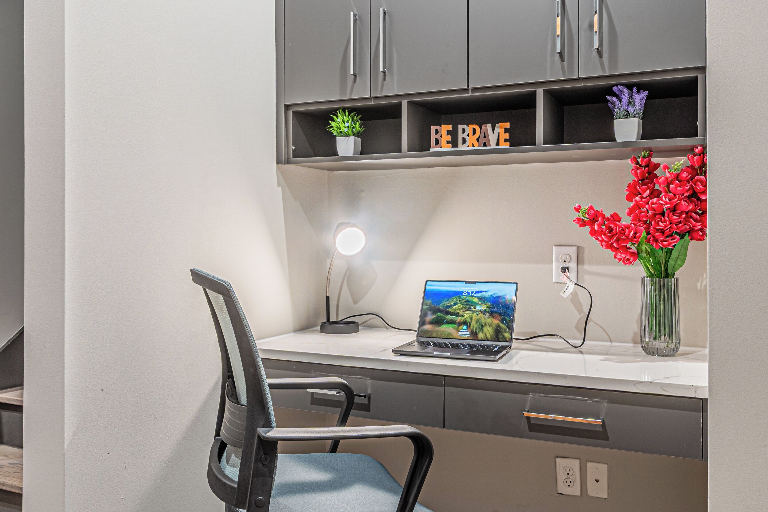 A modern office desk with a laptop, a desk lamp, and a vase of red flowers.