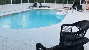 An outdoor swimming pool with a covered area, surrounded by black wicker chairs and a white fence. - High Springs Hideaway – 4BR w/ Pool & Bar • Near Springs & UF • Walk to Town (High Springs)