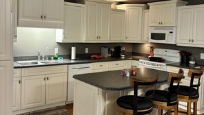 A kitchen with white cabinets, a microwave, a stove, and a bar area with stools. - High Springs Hideaway – 4BR w/ Pool & Bar • Near Springs & UF • Walk to Town (High Springs)