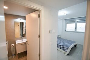 A bedroom with a bed, a window, a bathroom with a sink, and a mirror.