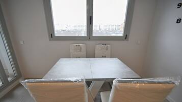 Una habitación con un ventanal grande, una mesa blanca y dos sillas cubiertas de plástico.