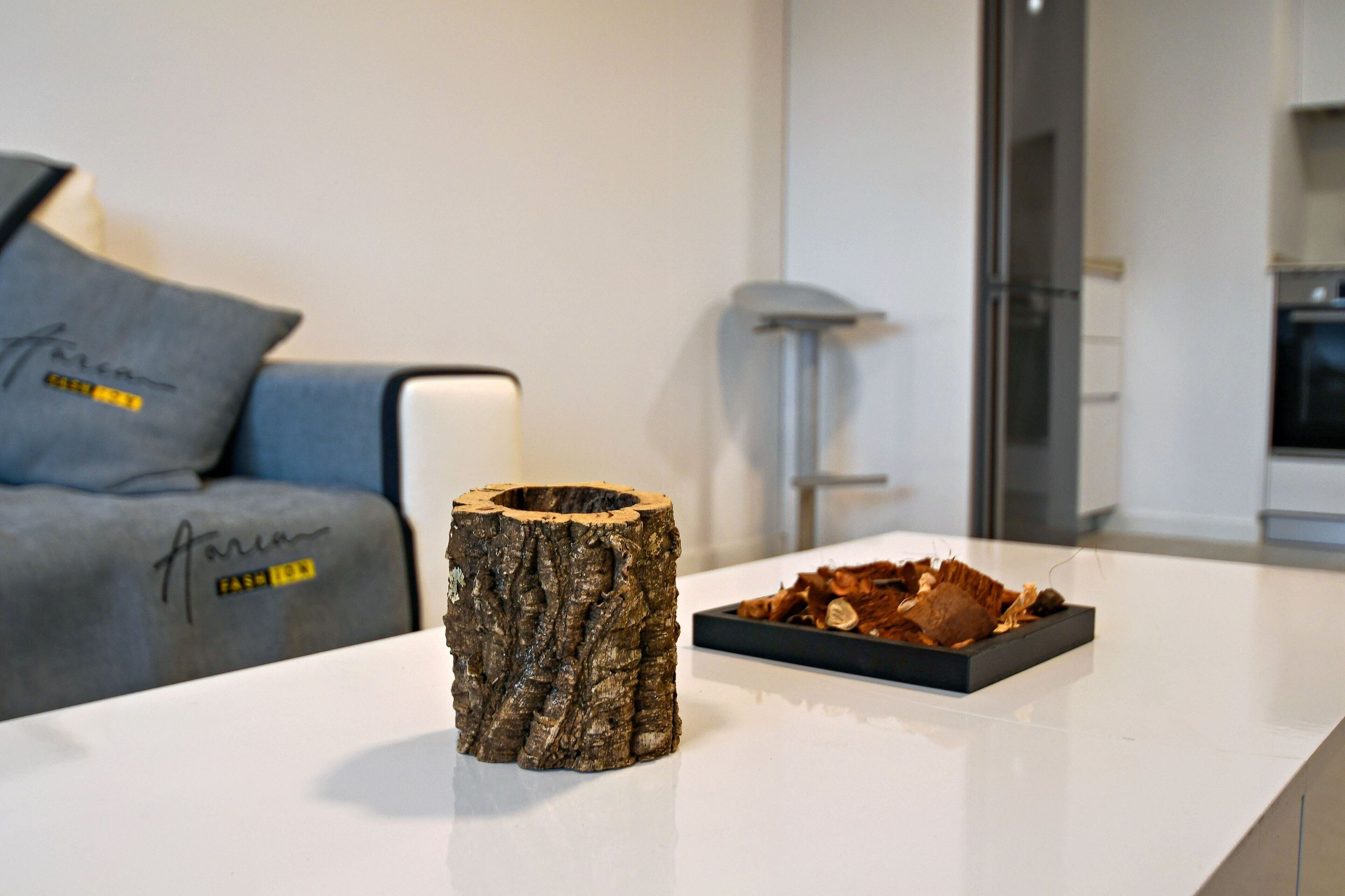Un salon moderne avec une table blanche, un canapé gris agrémenté d’un coussin décoratif et une sculpture en bois.