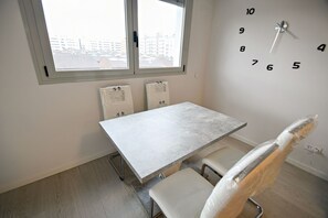 A room with a white table and chairs, a window with blinds, and a wall clock.