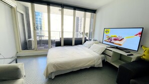 Ein Hotelzimmer mit Bett, Schreibtisch, Fernseher und einem Balkon mit Blick auf Gebäude.