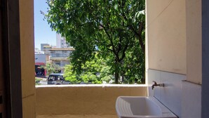Un baño con lavamanos y ventana con vista a una calle con edificios y un árbol.