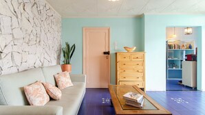 Una sala de estar con pared de piedra, un sofá con cojines estampados, una mesa de centro de madera y una puerta que da a una zona de cocina.