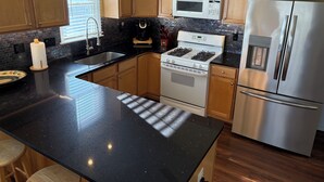 A kitchen with wooden cabinets, a black countertop, a stainless steel refrigerator, a microwave, a stove, and a sink.