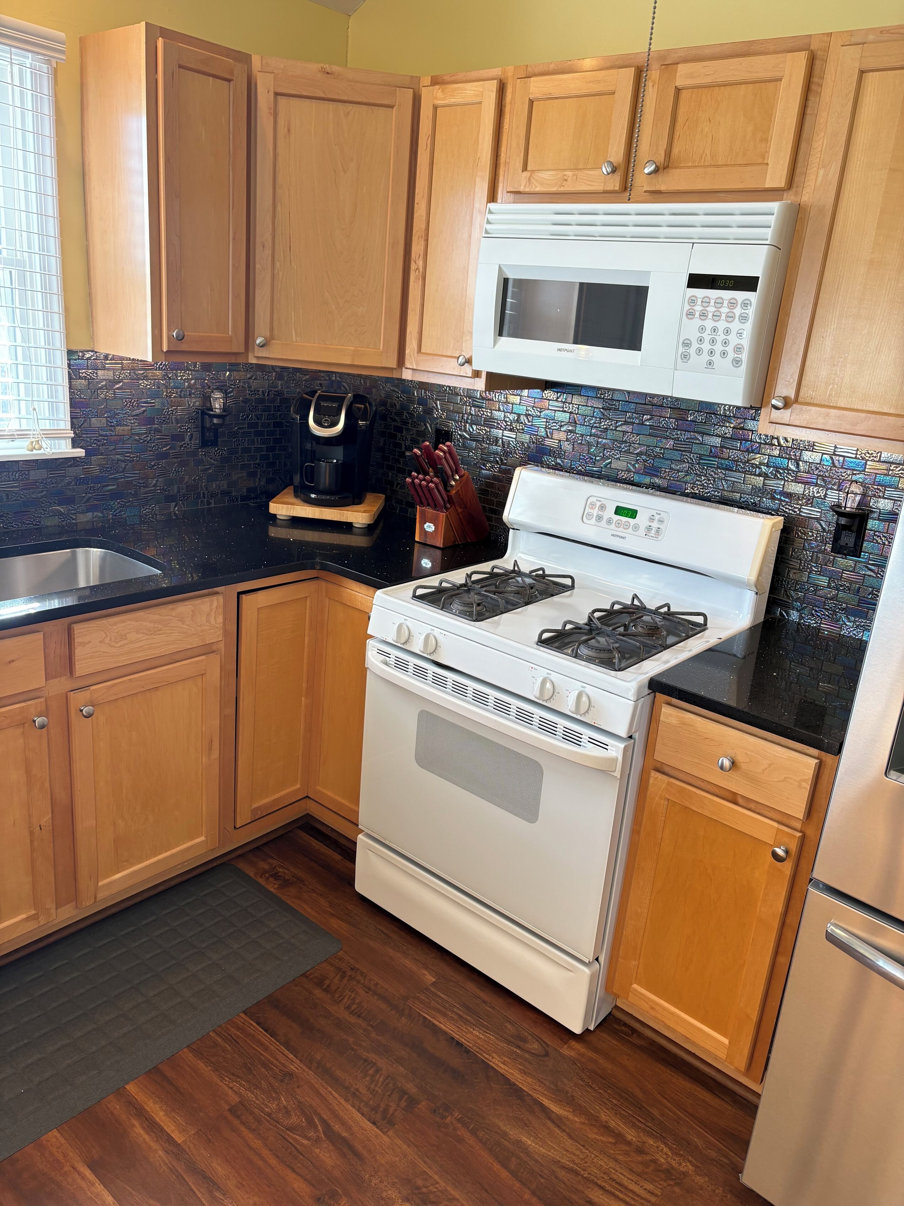 A kitchen with wooden cabinets, a black countertop, a white stove, a microwave, and a patterned backsplash.