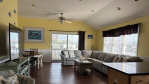 A living room with a sofa, a dining table with chairs, a TV, and a ceiling fan.