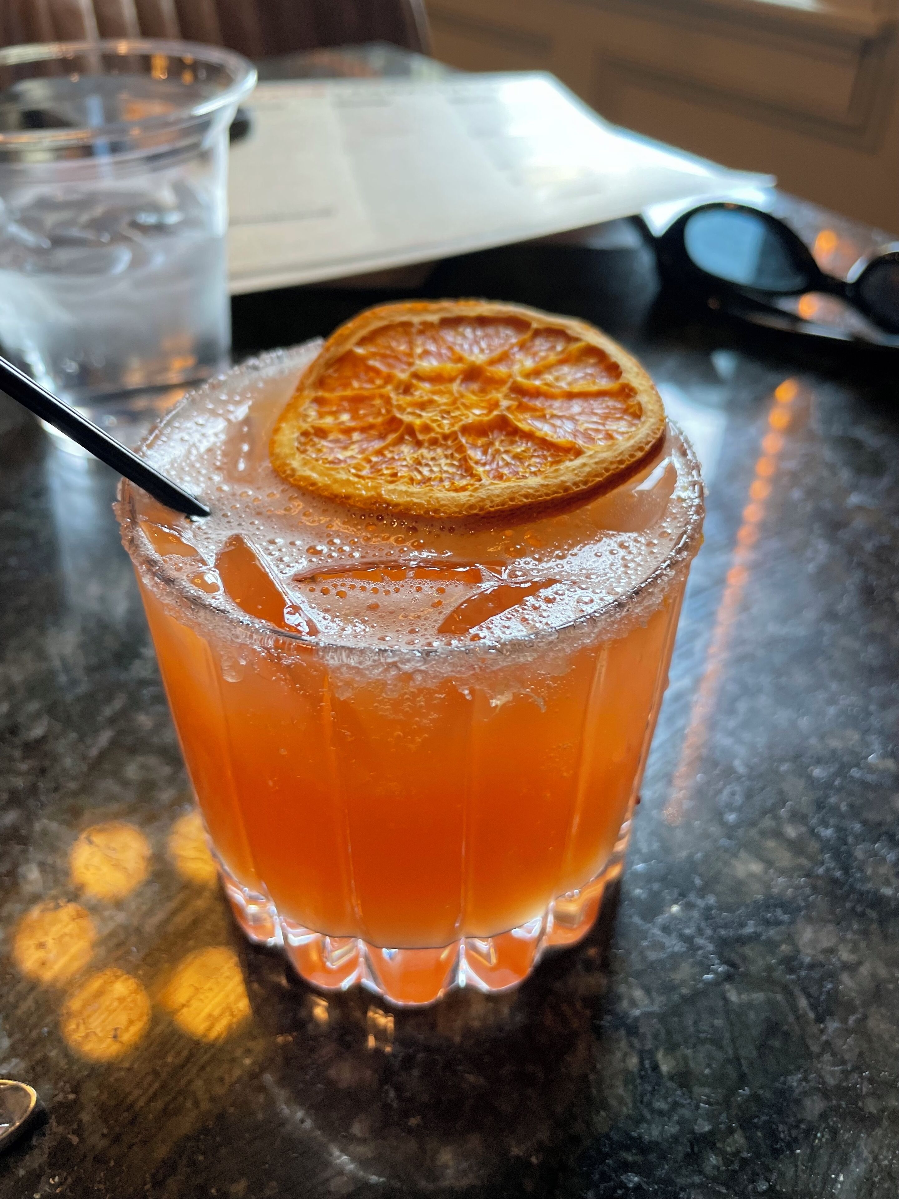 A glass of orange-colored drink with a slice of orange garnish on a table.