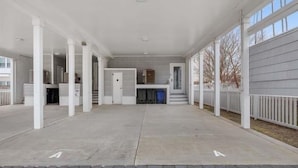 A covered outdoor area with a concrete floor, white columns, and a grey building in the background.