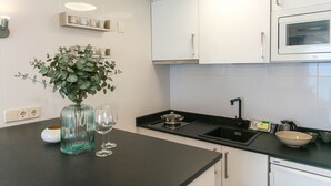 A modern kitchen with white cabinets, a black countertop, a built-in oven, and a vase with green plants. - WELCS ESTUDIO 237 PDA junto al mar (Platja d´Aro)