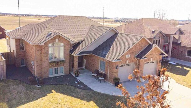 Une maison à deux étages, construite en briques, avec un garage, un patio couvert et un petit jardin à l’avant.
