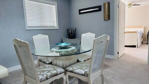 Un espace repas avec une table à plateau en verre, entourée de quatre chaises dotées d’assises rembourrées.
