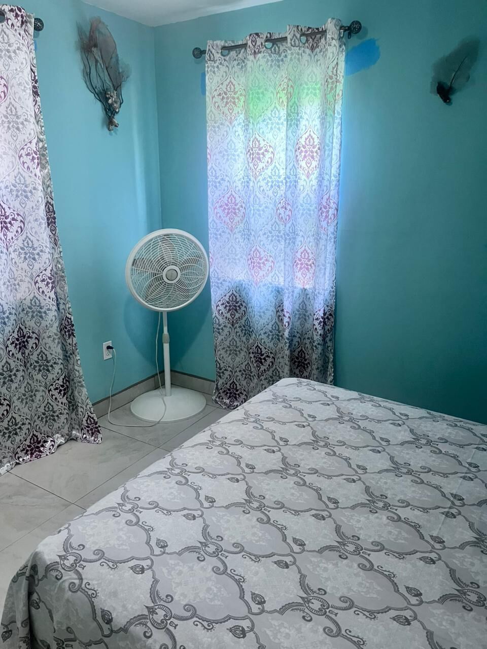 Quarto com cama, ventilador e cortinas estampadas.