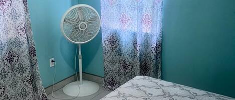 Quarto com cama, ventilador e cortinas estampadas.
