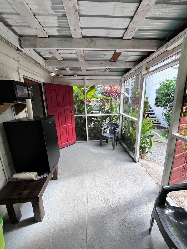 A covered patio area with a red door, a black TV stand, and a plastic chair. - Garden Lodge Hotel (Placencia)