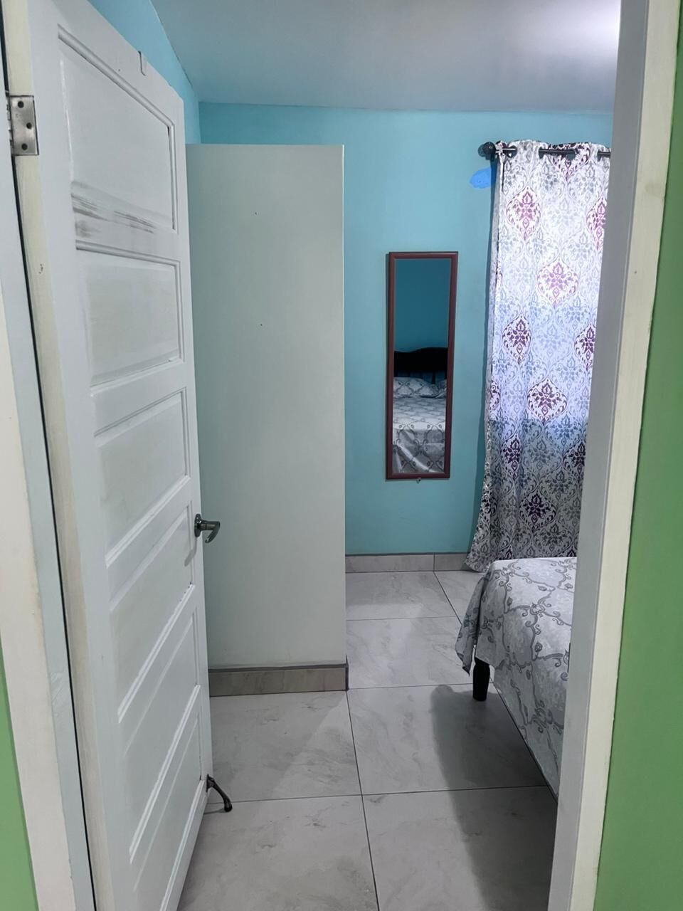 A room with a bed, a door, a mirror, and a curtain.