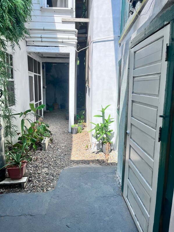 A narrow pathway leading to a garage, flanked by potted plants and a building with a white exterior.