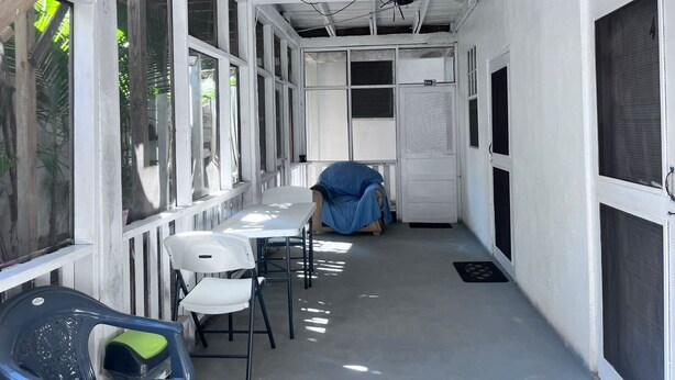 En overdækket gang med hvide vægge, et bjælkeført loft og en dør med et skilt.
