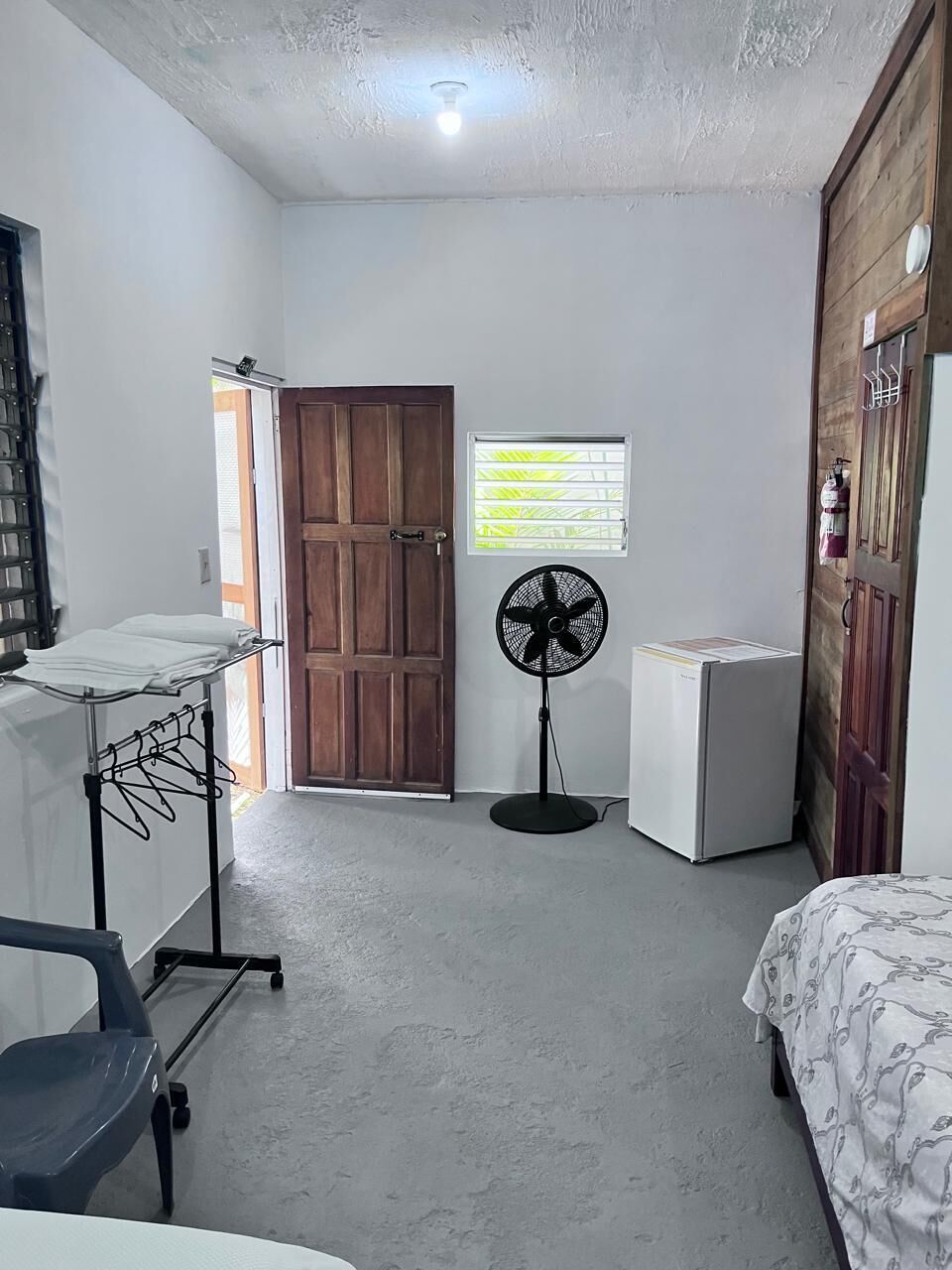 A bedroom with a bed, a fan, a small white appliance, and a wooden wardrobe.