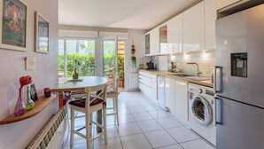 Une cuisine moderne avec des meubles blancs, un lave-linge encastré et un coin repas comprenant une table et des chaises.