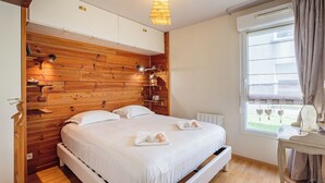 Une chambre à coucher avec une tête de lit en bois, un lit recouvert de draps blancs, une table de chevet et une fenêtre avec des rideaux.