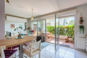 A modern kitchen with a wooden table, white chairs, and a dining area with a view of the garden. - Appartement Pont Pierre - Welkeys (Bayonne)