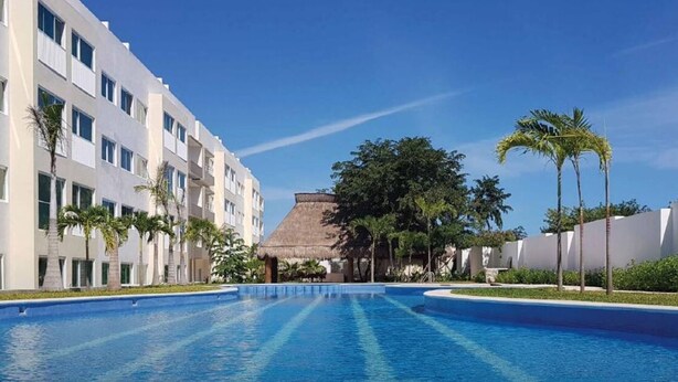 Una piscina con una struttura a tetto di paglia, palme e edifici moderni.
