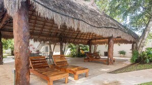 Zona relax esterna coperta con poltrone in legno e struttura a tetto di paglia.