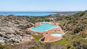 Ett semesterhotell med en stor pool i mitten, mindre pooler runt omkring och utsikt över havet.
