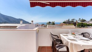 A terrace with a table set for dining, overlooking a coastal landscape with buildings and mountains. - Holiday Home 'Casa Centro' with Sea View, Wi-Fi and Air Conditioning (Mijas)