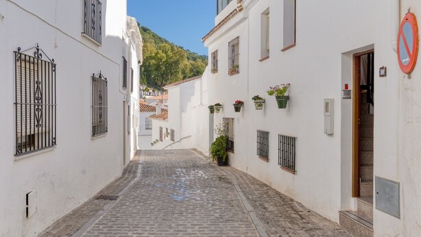 A narrow cobblestone street flanked by white buildings with barred windows and hanging flower boxes. - Holiday Home 'Casa Centro' with Sea View, Wi-Fi and Air Conditioning (Mijas)