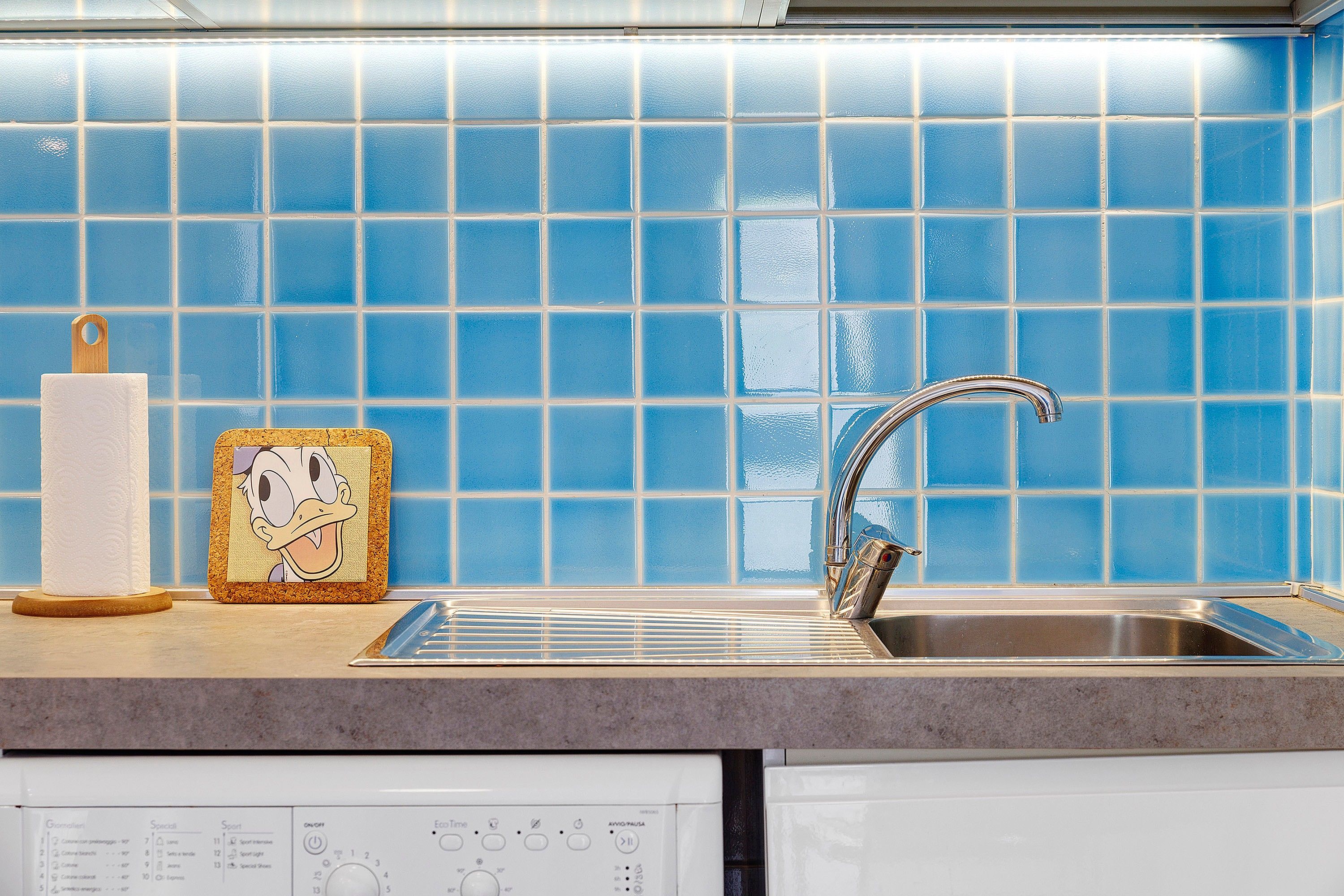 A kitchen with blue tiles, a stainless steel sink, and a paper towel holder.