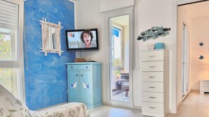 Una habitación con pared azul, televisión, mueble blanco y puerta que da a un espacio exterior.
