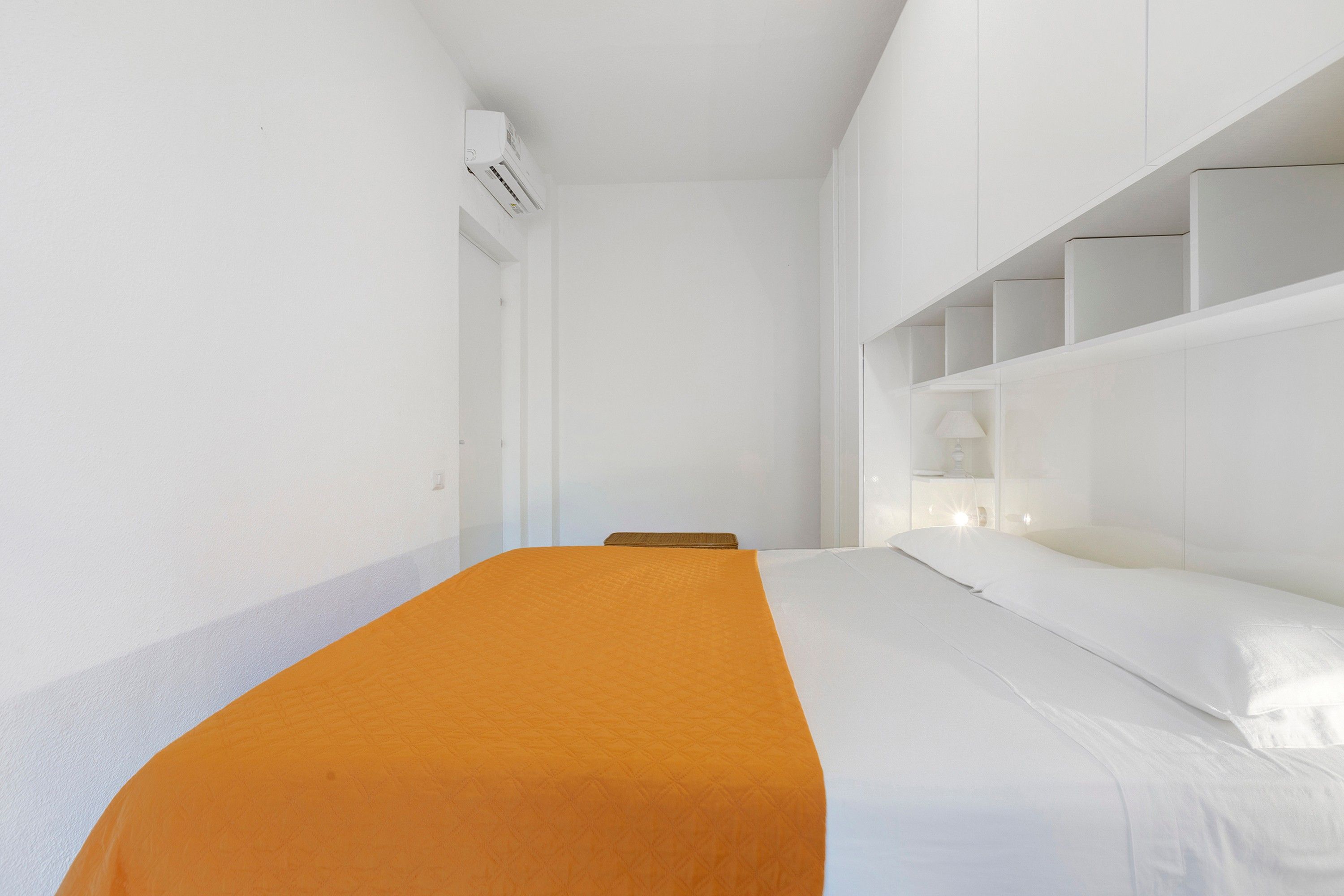 Una habitación de hotel con cama, mesita de noche, lámpara y estantería empotrada.