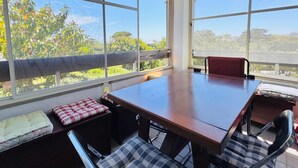 Una sala de estar con ventanales, una mesa grande y sillas, y vistas a zonas verdes.