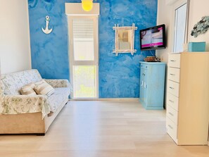 Une pièce avec un canapé à motifs floraux, un mur bleu, un meuble en bois et un téléviseur.
