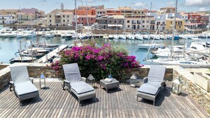 Un puerto deportivo con barcos, una terraza de madera con sillones de descanso y un muro de piedra con flores.