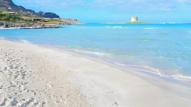 Una playa con agua cristalina, una orilla de arena y una torre en una pequeña isla.