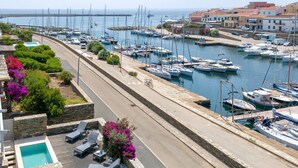 Un puerto deportivo con barcos, una piscina con sillas de descanso y una carretera aledaña.